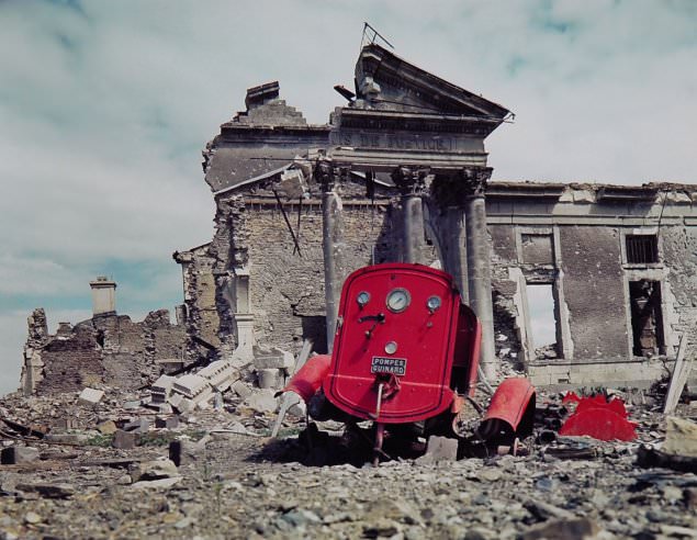 #11 View of the ruins of the Palais de Justice in the town of St. Lo, France, summer 1944. The red metal frame in the foreground is what’s left of an obliterated fire engine