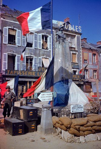 #25 American troops stand beside a World War 1 monument bedecked with French flags after the town (exact location unknown) was liberated from German occupying forces, summer 1944