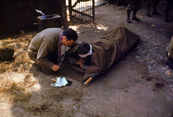 #6 An American Army chaplain kneels next to a wounded soldier in order to administer the Eucharist and Last Rites, France, 1944