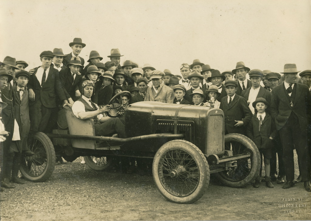 #34 Man seated in a modified Overland racing car surrounded by crowd