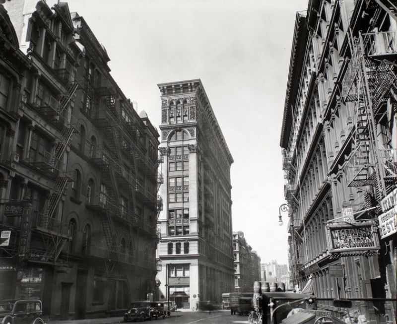 #2 Broadway near Broome Street, Manhattan. Looking down Broadway, ornate Bank of Sicily Trust near center of image, sign for vegetarian restaurant, right, cars and trucks.