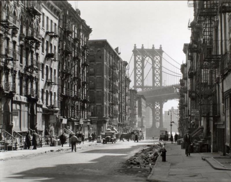 #24 Looking down Pike Street toward the Manhattan Bridge, street half in shadow, rubble in gutters, some traffic.