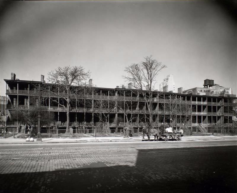 #32 Rhinelander Row: I. Seventh Avenue between 12th and 13th Streets, Manhattan. Row of houses lined with wooden porches, wagon in front, cobblestone street with trolley tracks.