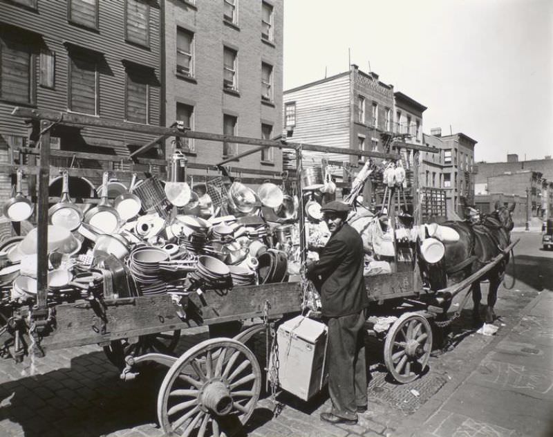 #37 Tinker looks over his shoulder at camera while he ties box to wagon already loaded with pans, brushes, basins, etc.