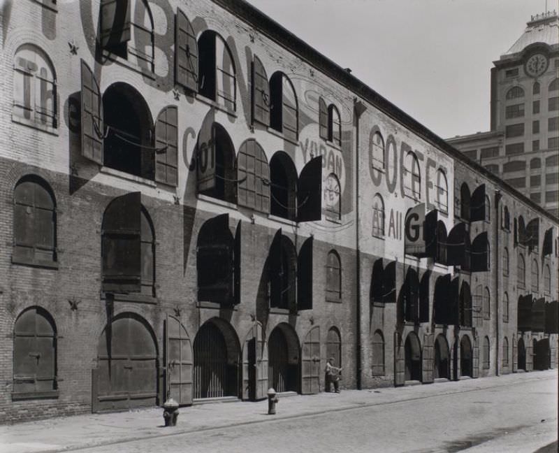 #38 Warehouse, Water and Dock Streets, Brooklyn. Four-story brick warehouse with arched windows and doors, some of which are open, partially hiding the Yuban Coffee advertisement painted on it.