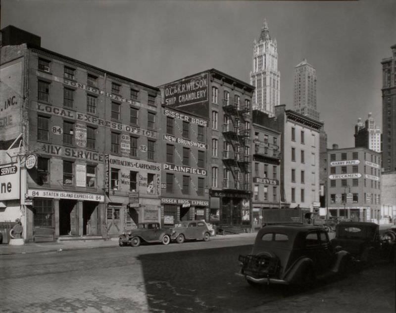 #45 Dey Street between West and Washington Streets, Manhattan. Express companies, ships’ outfitters and a contractor fill 4 and 5 story buildings along Dey St., tall towers beyond in upper right.