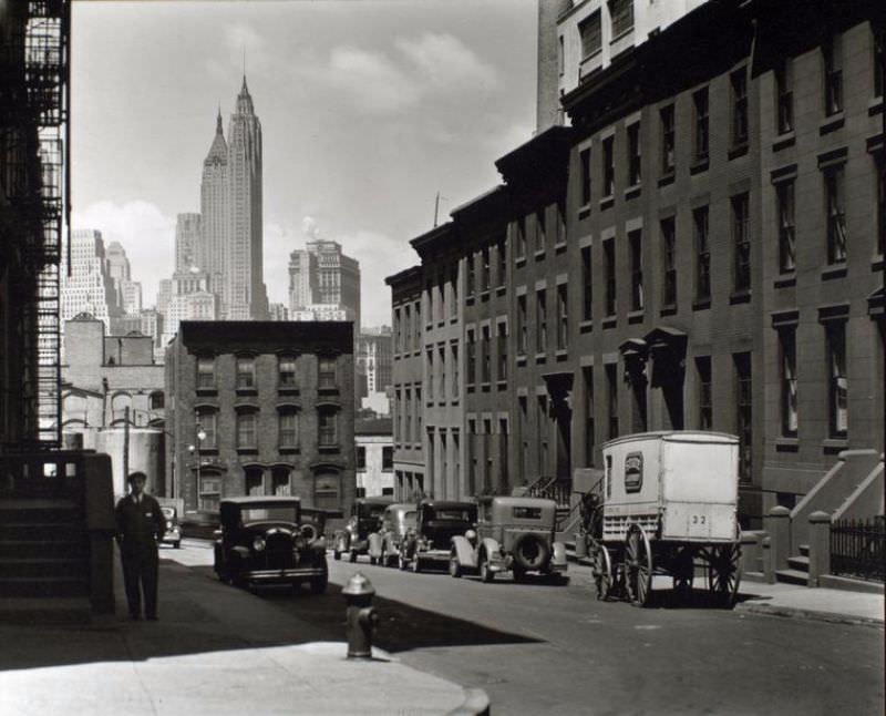 #56 Willow and Poplar Street, looking east [sic, view is actually looking toward Manhattan], Brooklyn. Laundry wagon, cars, along sloping street lined with rowhouses, skyline of Manhattan visible above buildings at end of the street.
