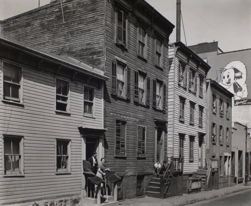 #59 Talman Street, no. 57, Brooklyn. Man talks to woman with broom in hand on stoop of clapboard house, boys next door sit on stoop, Eskimo pie sign on building at right.