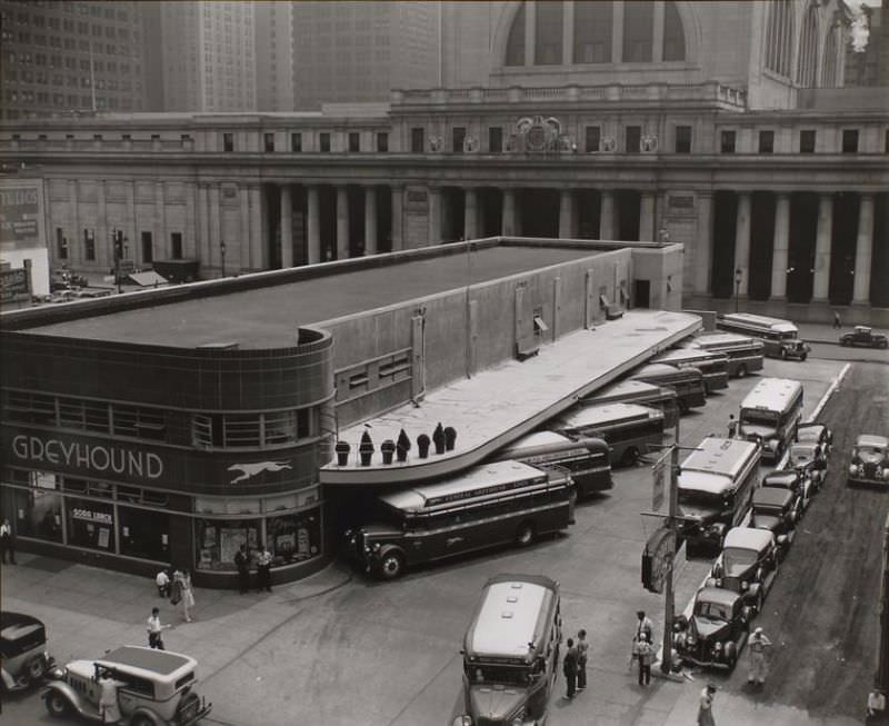 #64 Greyhound Bus Terminal, 33rd and 34th Streets between Seventh and Eighth Avenues, Manhattan. View of the terminal from above, showing buses, two story station with curved corners; cabs in foreground, Penn station beyond.