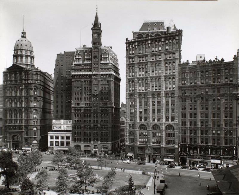 #67 Looking across City Hall Park at buildings lining Park Row, including the Tribune and Pulitzer buildings and the statue of Franklin.