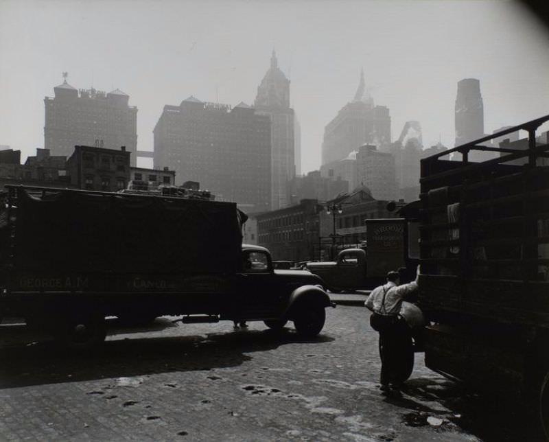 #68 City Vista, West Street, looking east, Manhattan. Men and trucks in foreground, Hudson Terminal and other buildings in the haze beyond.