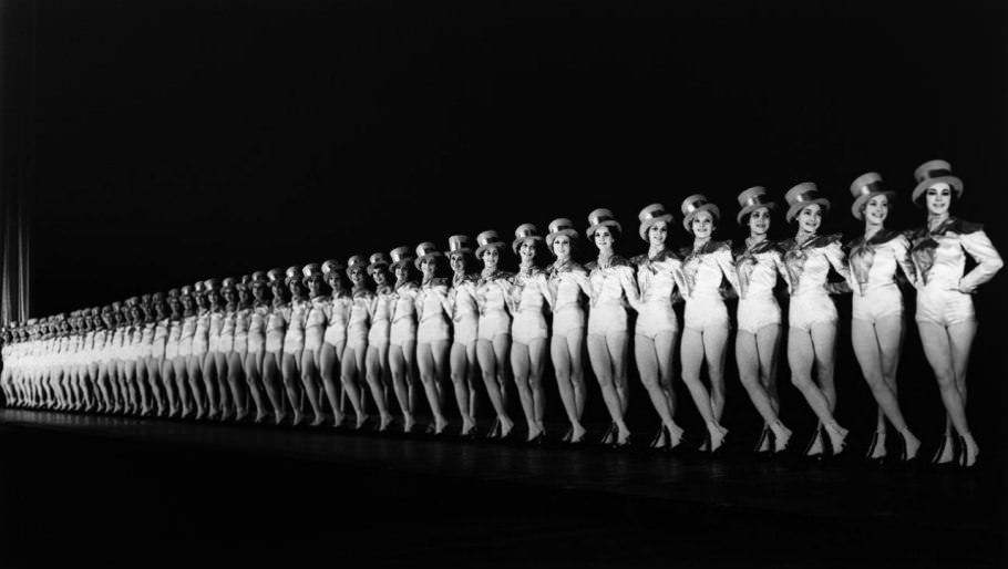 #57 Onstage in 1937, the Rockettes cut a sharp, diagonally receding line—in white and top hats—against the dark backdrop. Originally just one line of dancers, the Rockettes today encompass two 40-girl casts.