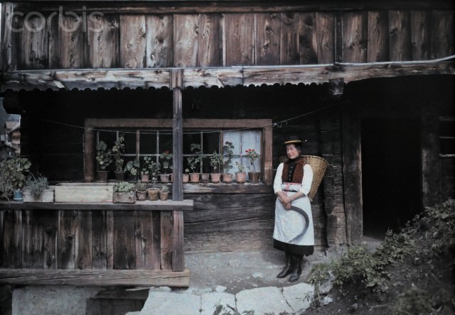 #14 A woman standing outside a house with a scythe and basket, Heiligenblut, Austria, 1929.