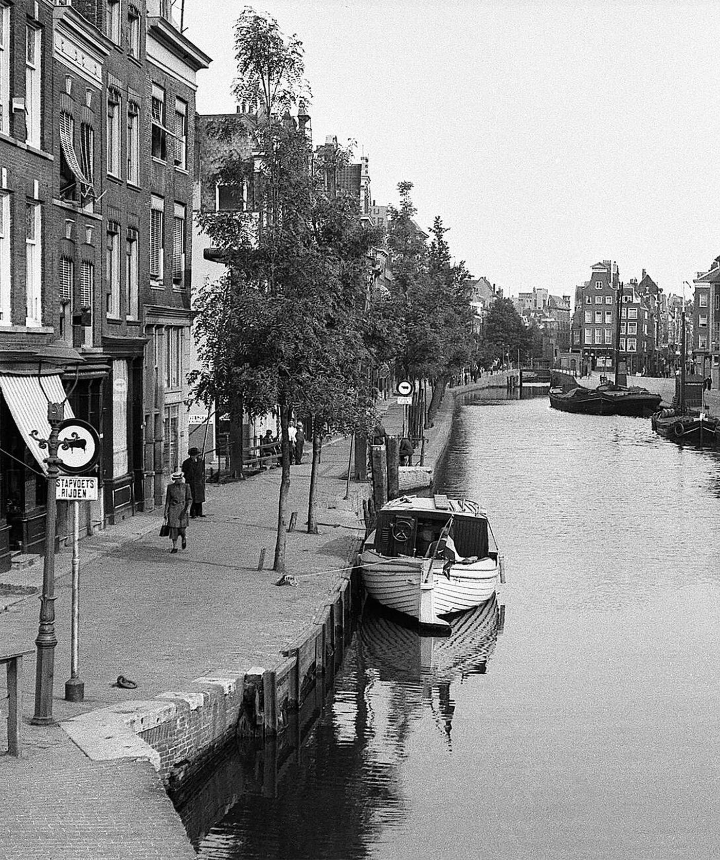#52 Canal-side scene in Amsterdam, Holland, with pedestrians and barges, 1930s.