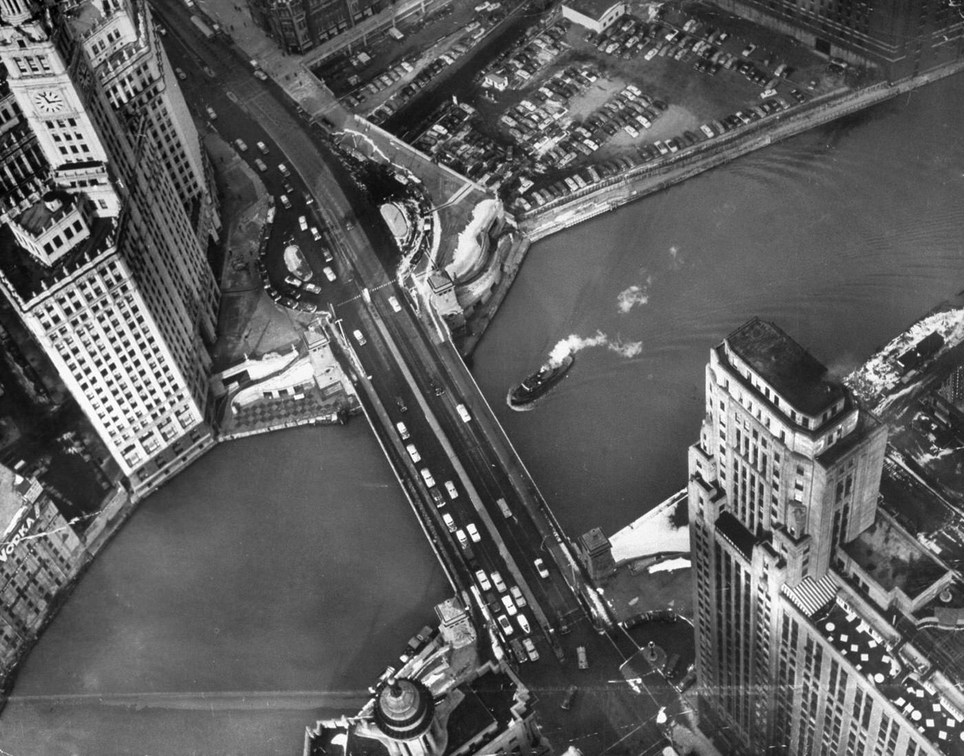#11 Chicago’s famous Wrigley Building looks like candy castle from a helicopter above spire. Building is split in two parts and a railroad track runs between them. Behind them is Chicago River, with Michigan Avenue bridge.