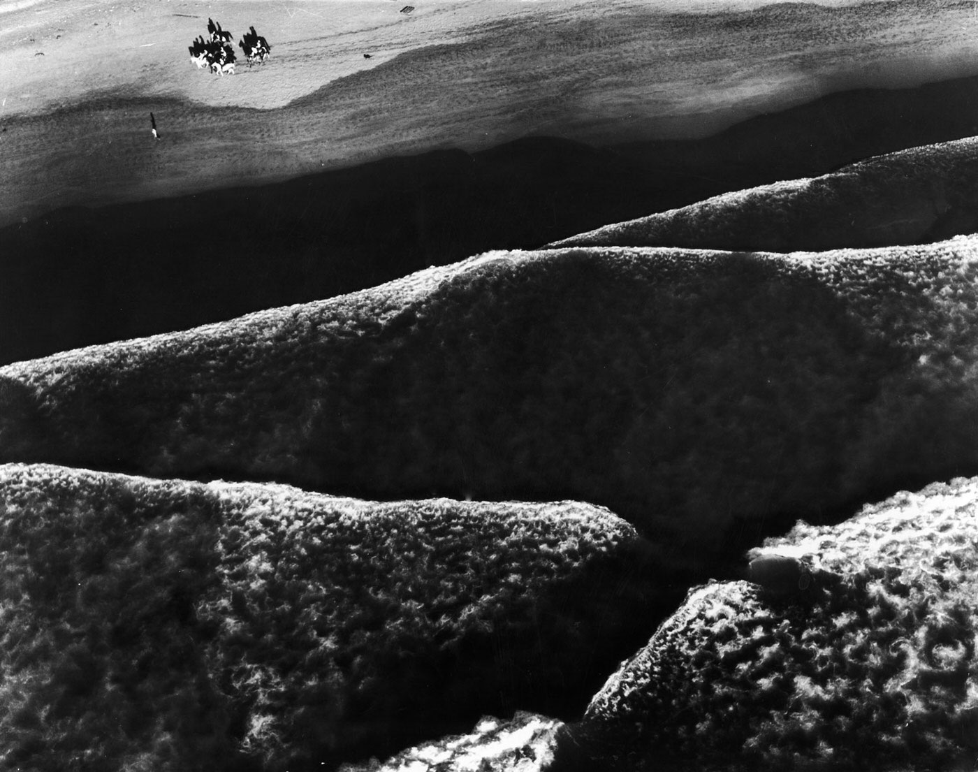 #20 Beach riders guide their horses along the shore at high tide at Ocean Beach, near Fort Funston, California, as the long, low Pacific rollers make mountain like patterns of the surf.