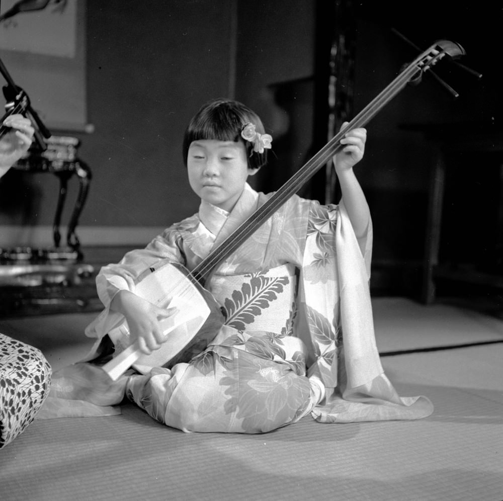 #5 A young girl in a geisha kimono playing the samisen, 1950s.