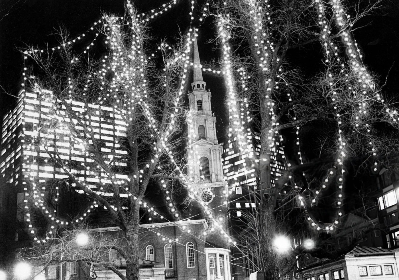 #47 The Park Street Church is framed by Christmas lights in the trees on Boston Common, 1974.