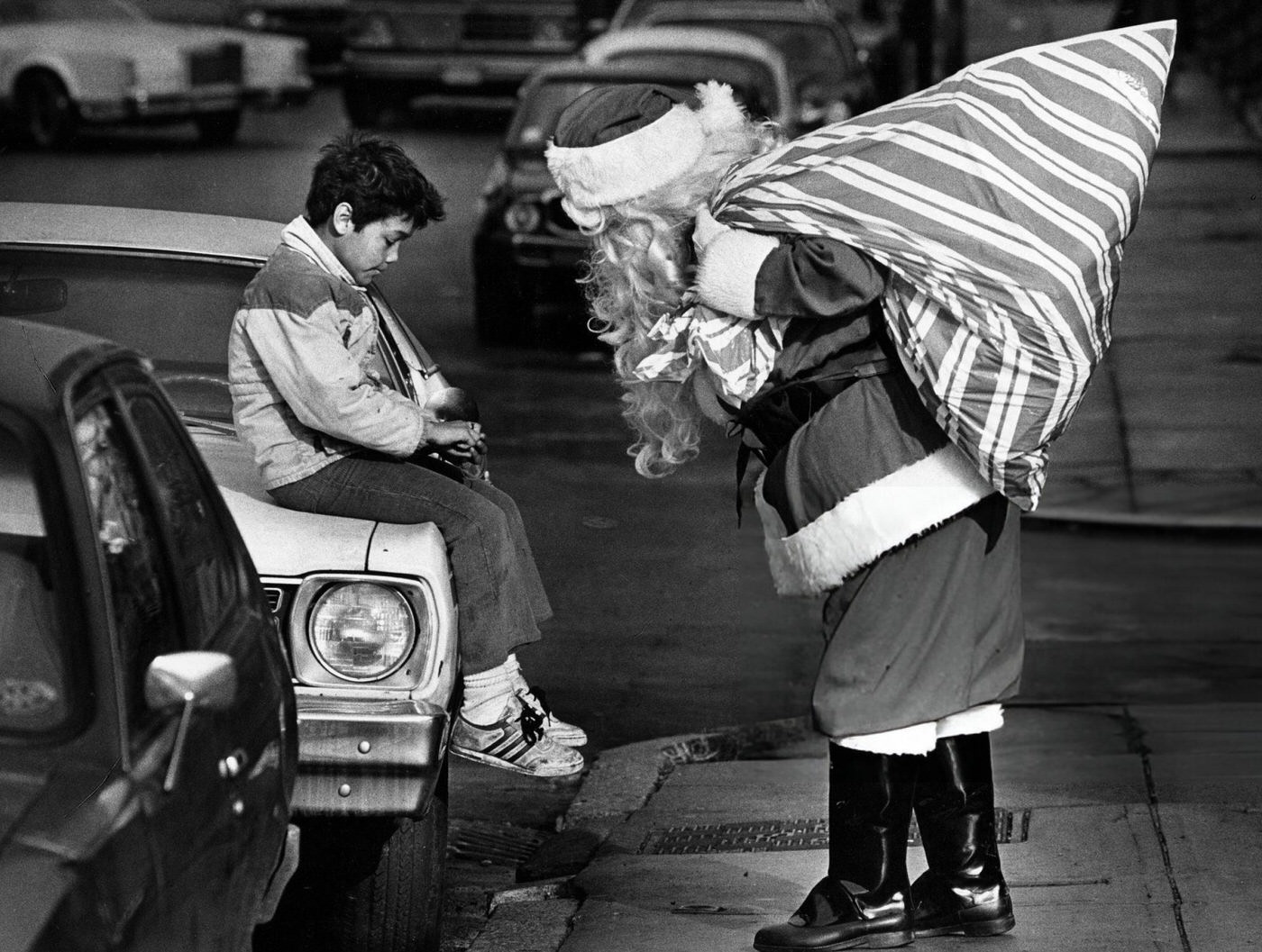 #56 Santa Claus stops to inspect a cut on a boy’s finger while delivering presents for homeless children in Boston, 1985.
