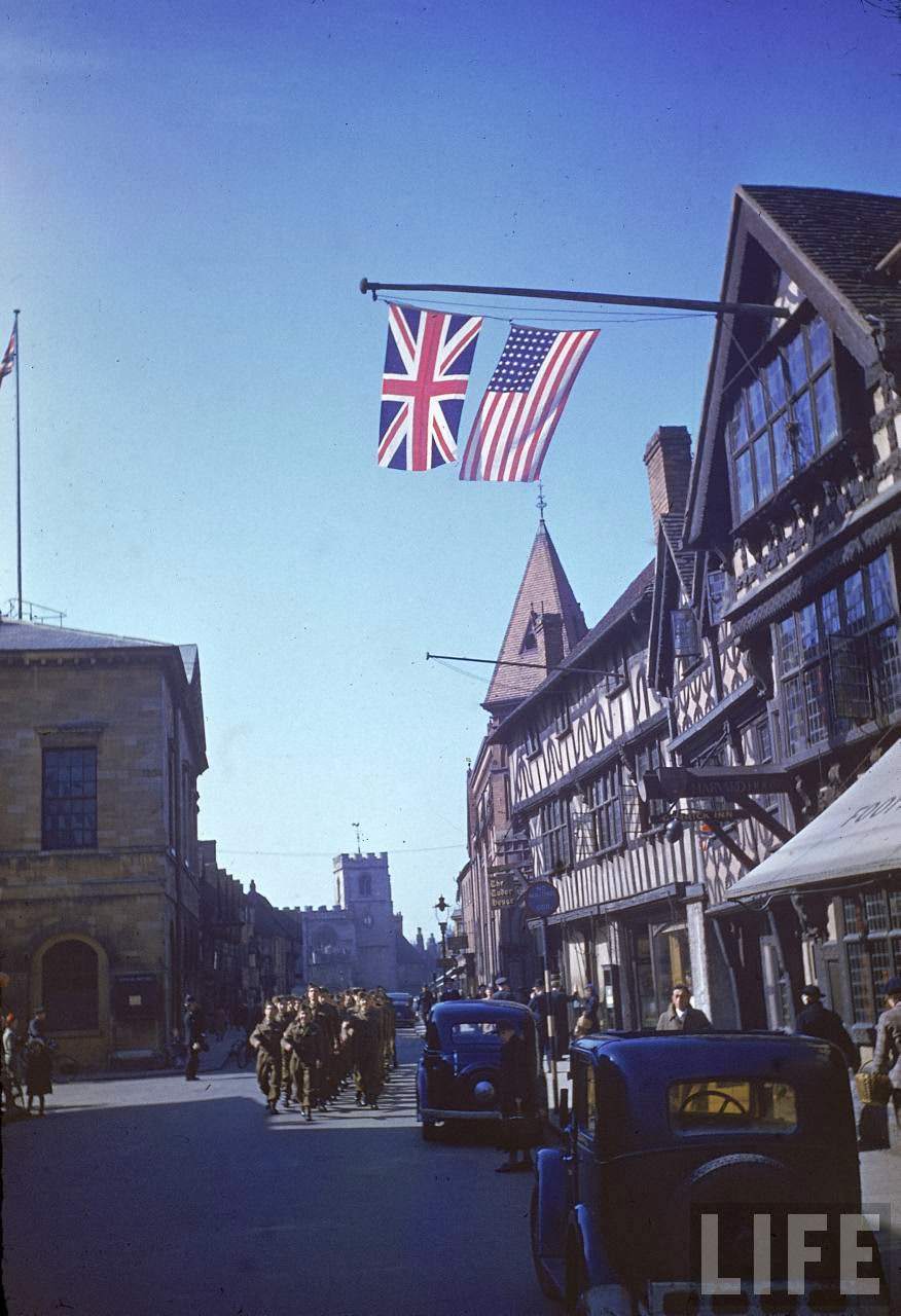 British and American flags flying from building as US Army band leads procession to Holy Trinity Church during birthday celebrations honoring William Shakespeare.