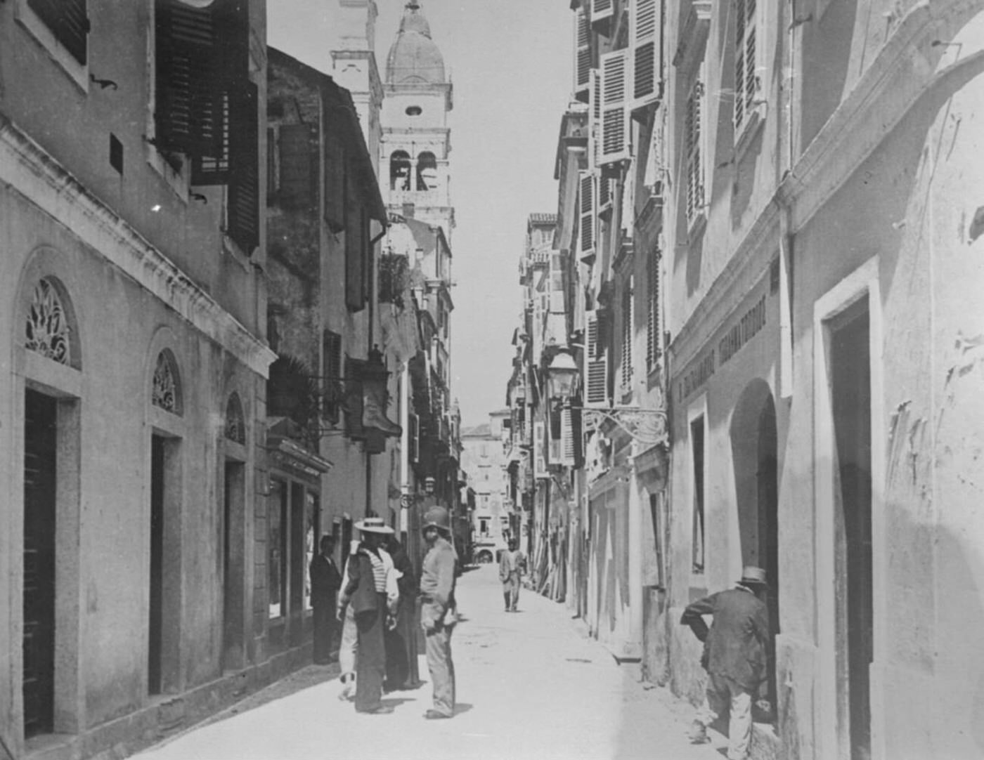 #66 A typical street in Corfu, the Calle S Spiridione, with a figure bearing a resemblance to a London policeman, 1923.