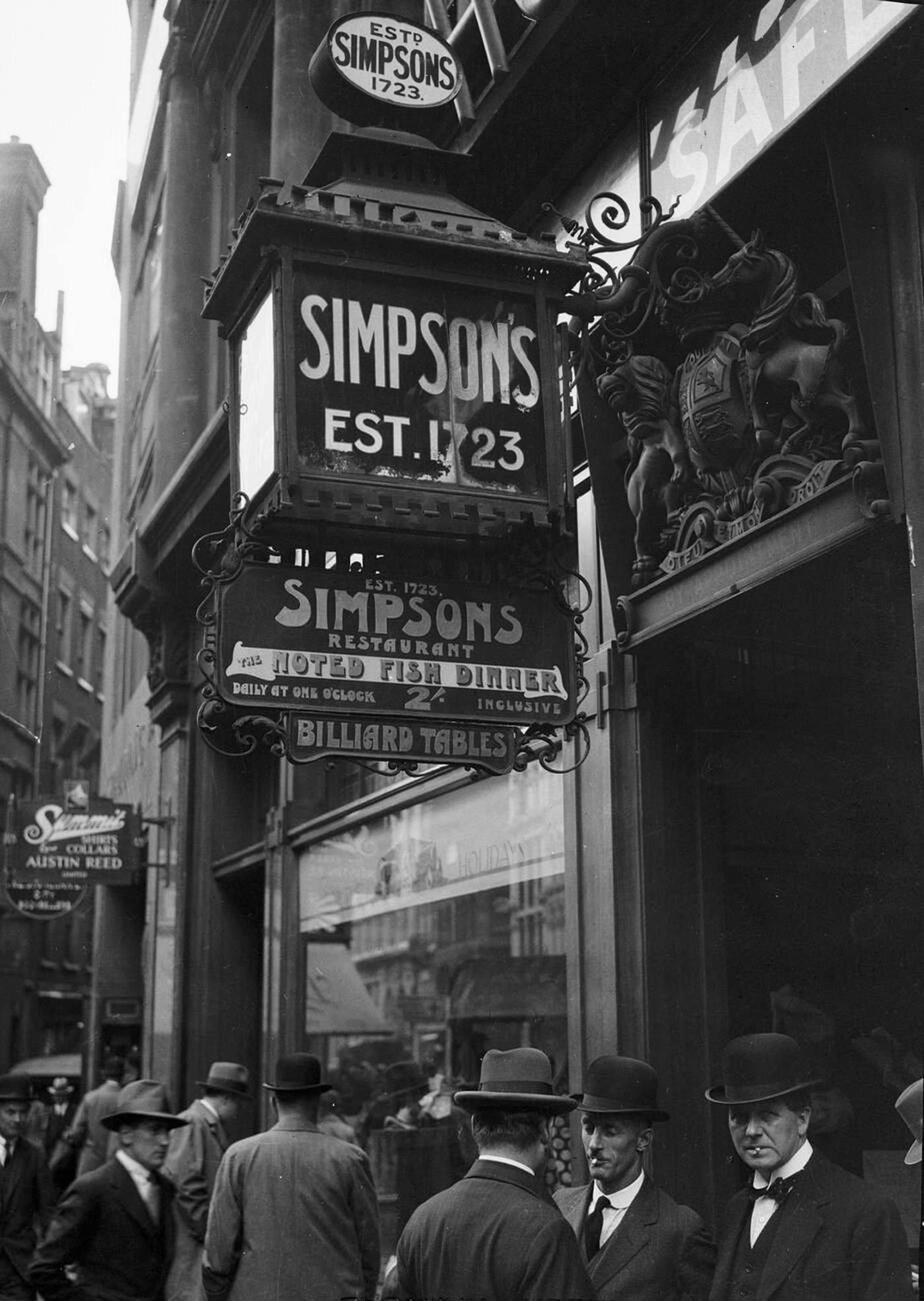 #51 Men stand outside Simpson’s Restaurant, London, with signs indicating the restaurant was established in 1828, 1921.