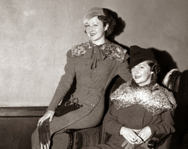 #5 Model Mona Mora (l.) wears a gray woolen coat dress with a removable sailor collar, and Lee Sherman (r.) wears a bright green tweed fall suit with a matching gray krimmer fur high crown fabric hat at a 1933 fashion show at Hotel Pennsylvania.