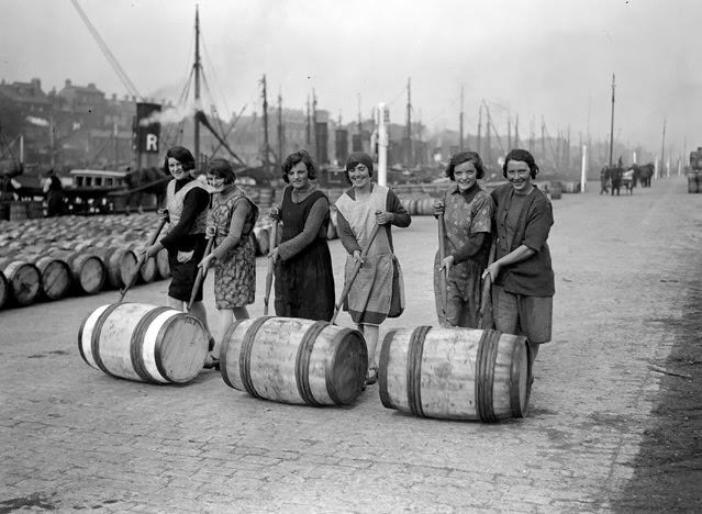 #9 Yarmouth fisher-girls push barrels of herring along the quayside using long poles, 1929.
