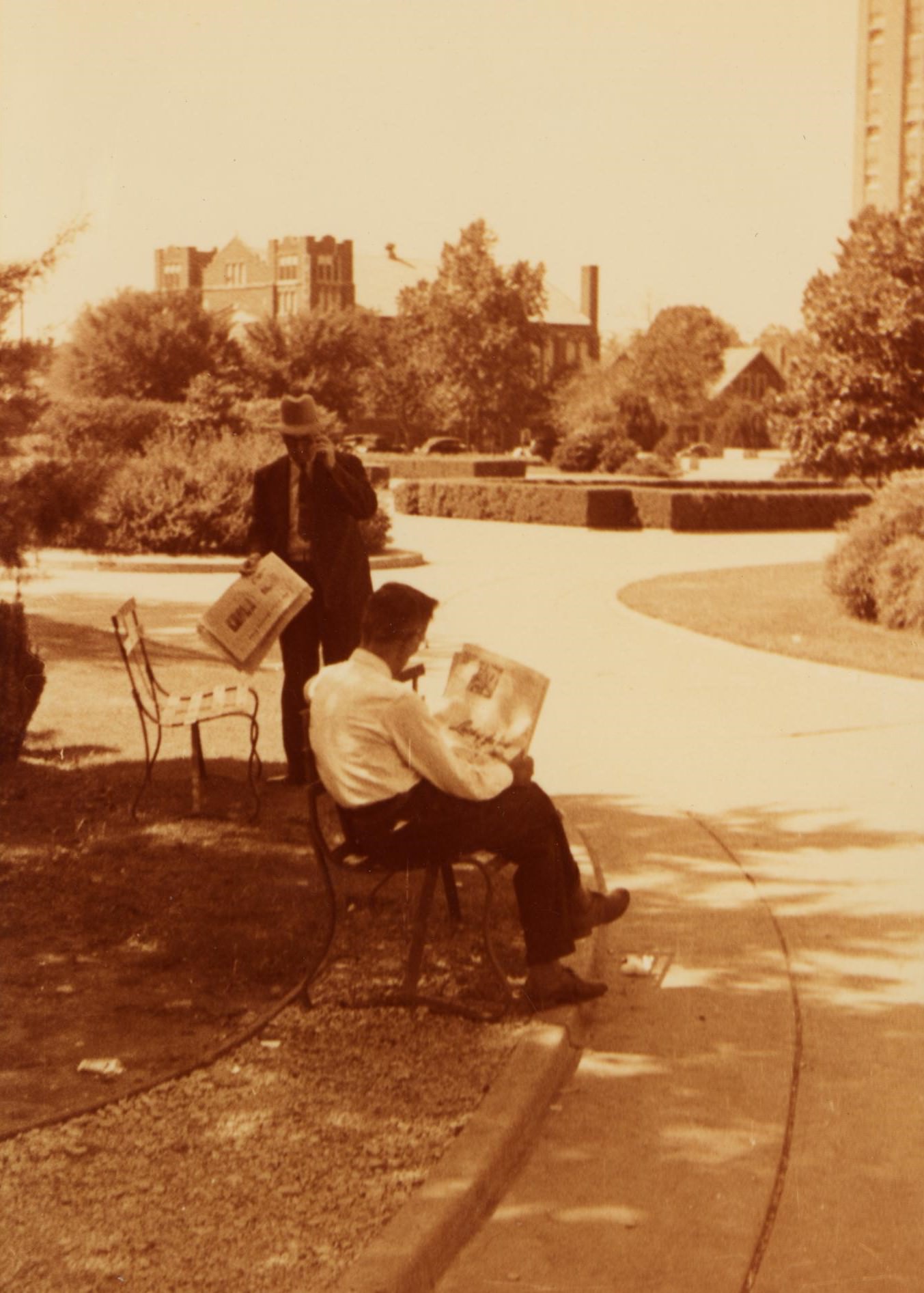 #114 Two men reading a newspaper in a park, 1930s.