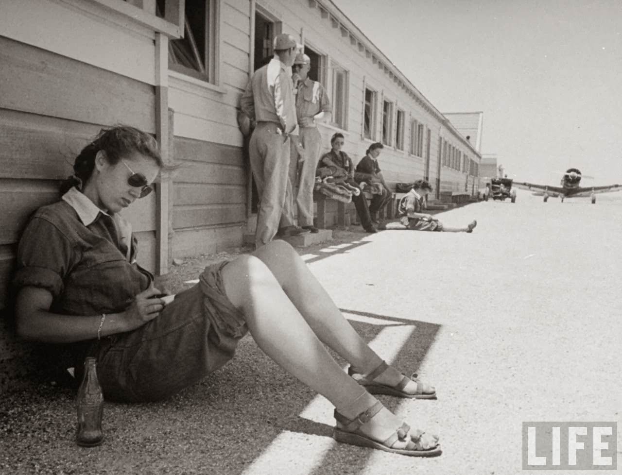 #10 Madge Rutherford, pilot trainee in the Women’s Flying Training Detachment, writing letter home w. a finished Coca Cola by her side as she leans against barrack while waiting for her flight period on basic line, at Avenger Field.