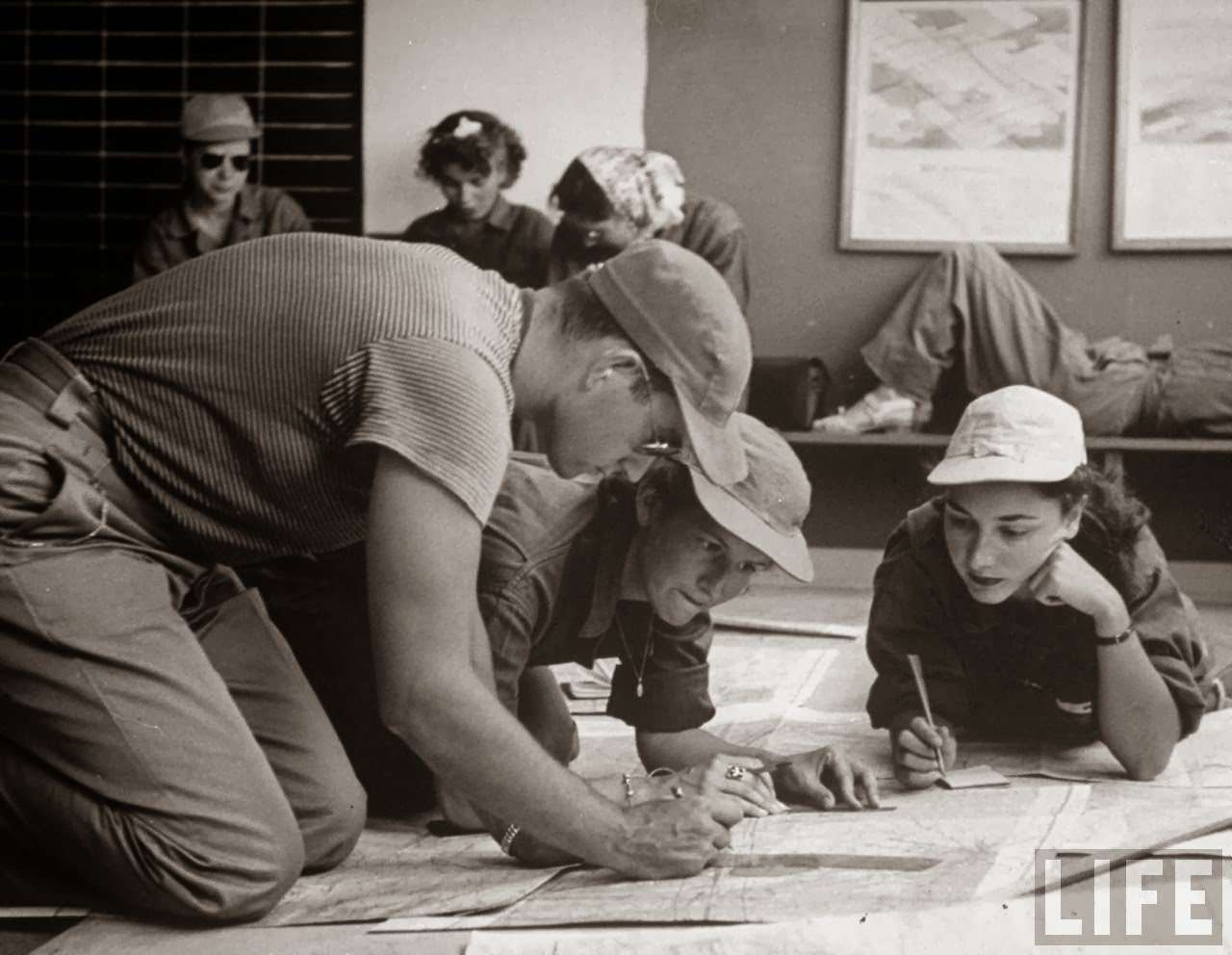 #15 Janet Zuchowski (C) & Alice Jean May, (R) pilot trainees in Women’s Fllying Training Detachment, on floor ploting cross-country flight on a map w. Norman Schaeffer (L) who helps them as one of the civilian flight instructors, at Avenger Field.