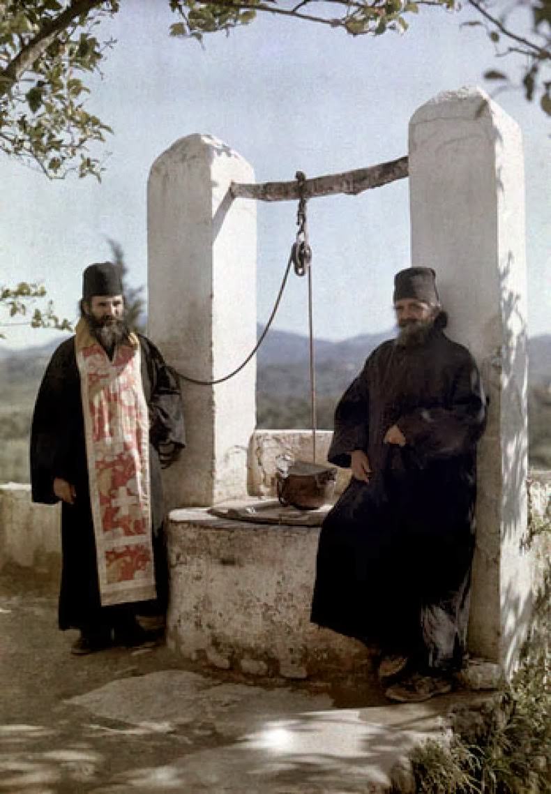 Prior and his monk stand next to well at Europulus monastery, Corfu.