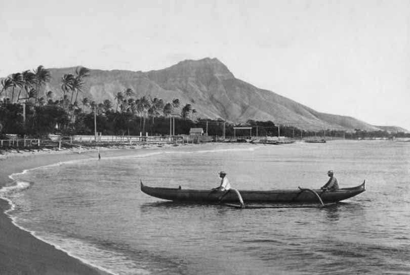 #86 Two local men in their raft rest by the beach at Waikiki Bay with Diamond Head in the background, 1900s.
