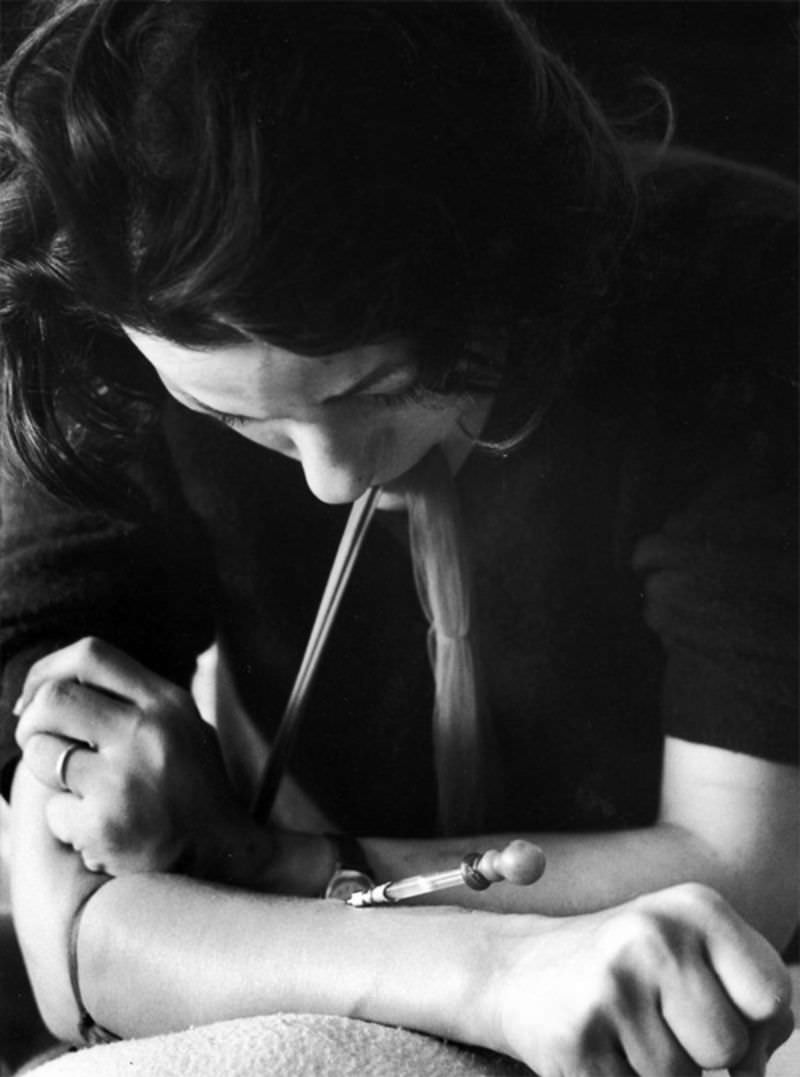 #11 Karen with nylon stocking around her arm to make vein pop out as she uses hypodermic needle on an eyedropper which addicts call a “spike” to shoot up with heroin.