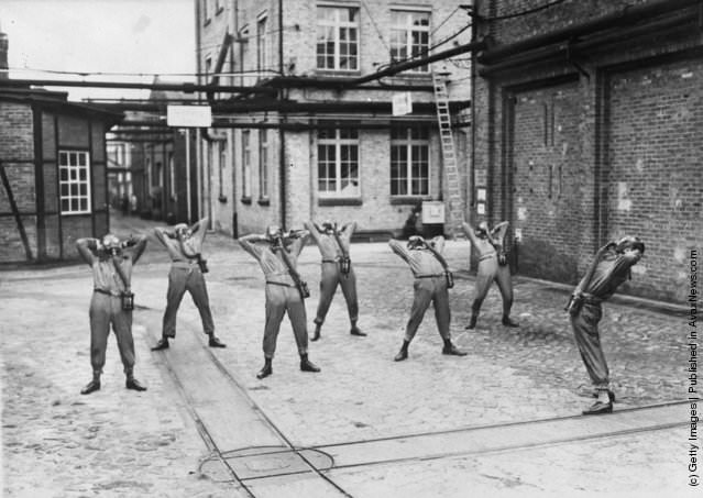 #8 Men wearing gas masks exercising in a factory yard, 1935.