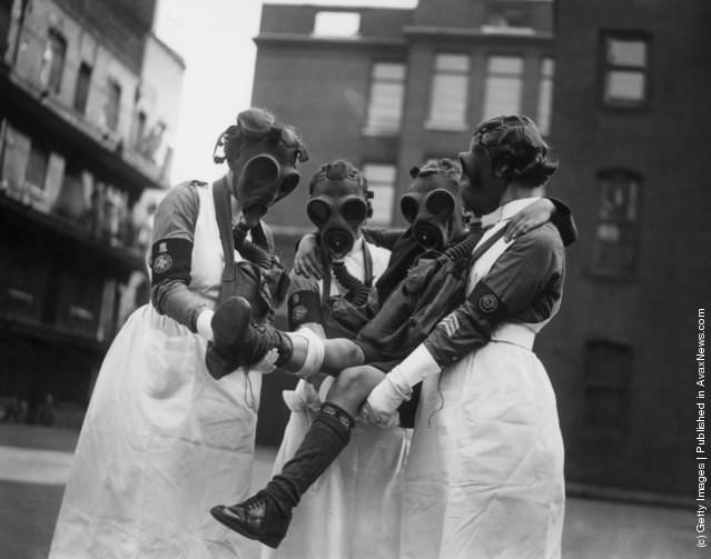 #13 Nurses in gas masks attending a patient during a gas attack demonstration in London, 1935.