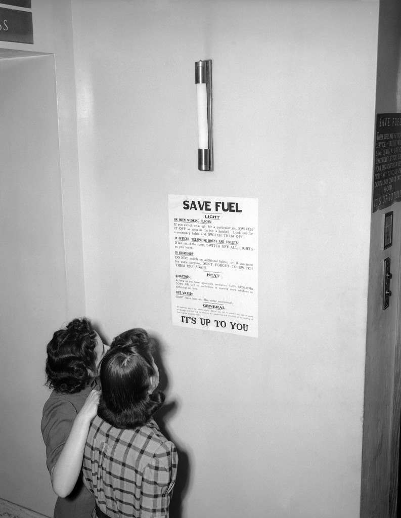 #16 Two London office workers read the fuel economy notice displayed on every floor of the building, 1943.