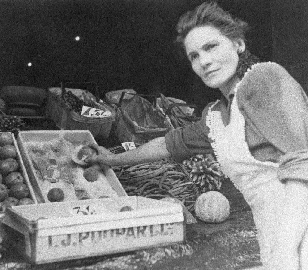#20 A fruit vendor demonstrates that small peaches cost a dollar each in London, 1944.