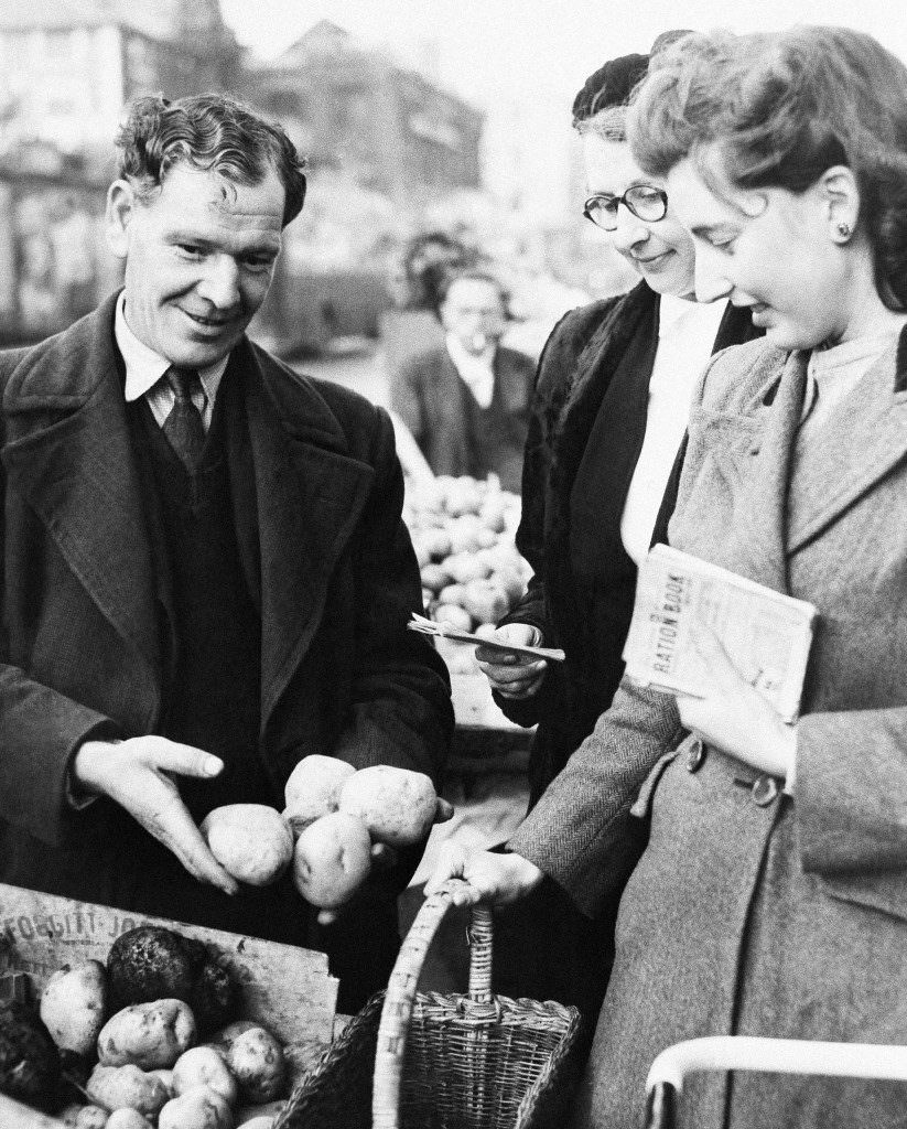 #26 Mrs. Anne Allen receives her weekly ration of potatoes from a street vendor in Kilburn, North London, 1947.