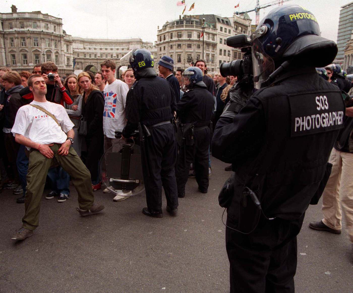 #67 An anti-capitalist demonstrator being photographed by police in Trafalgar Square, 2000.