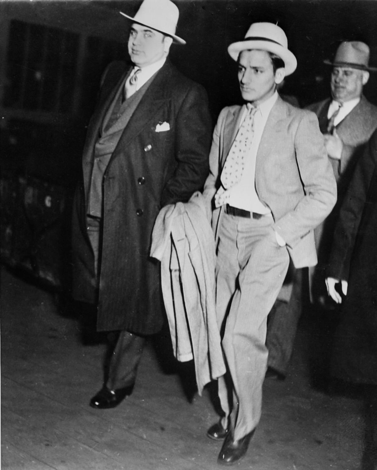 #25 Capone handcuffed to a convicted automobile thief being marched through a train station in Chicago to board a special car to Atlanta Penitentiary, May 3, 1932.
