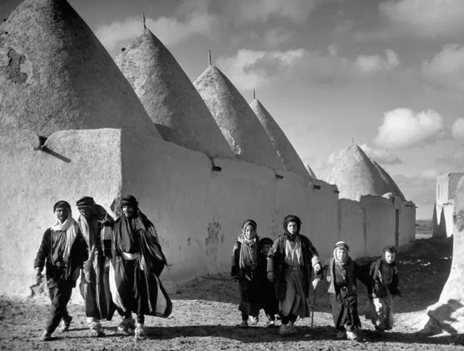 #16 A family walks past the walled town and beehive-shaped homes of Tell Bisse, Syria, 1940