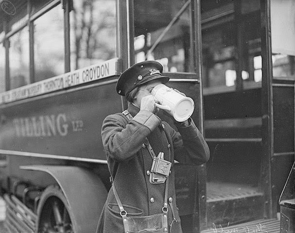 #14 A women bus conductor has a warming drink of hot milk beside her south London bus, 1916.