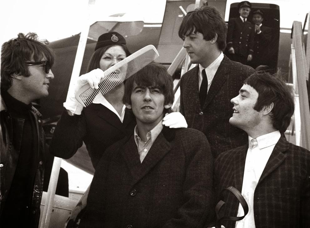 #30 George Harrison gets the big comb treatment from BOAC stewardess Anne Creech, after their arrival at Windy airport in London; John Lennon, Paul McCartney and drummer Jimmy Nicol, who stood in for Ringo Starr for the trip to The Netherlands are also pictured, 1964.