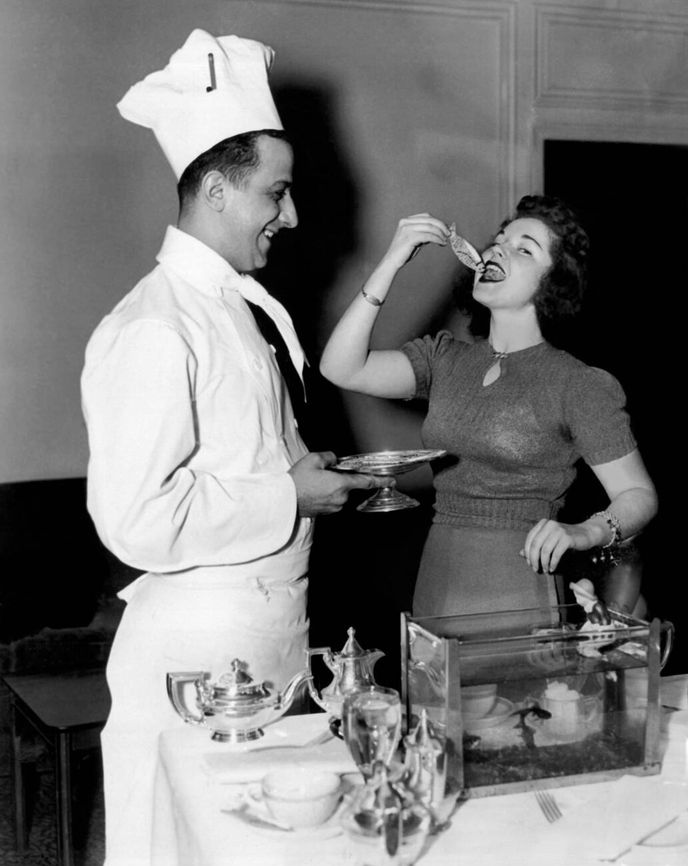 #69 A Kappa Kappa Gamma sorority member at Boston University tries eating a goldfish made of cake at the Statler Hotel, 1939.