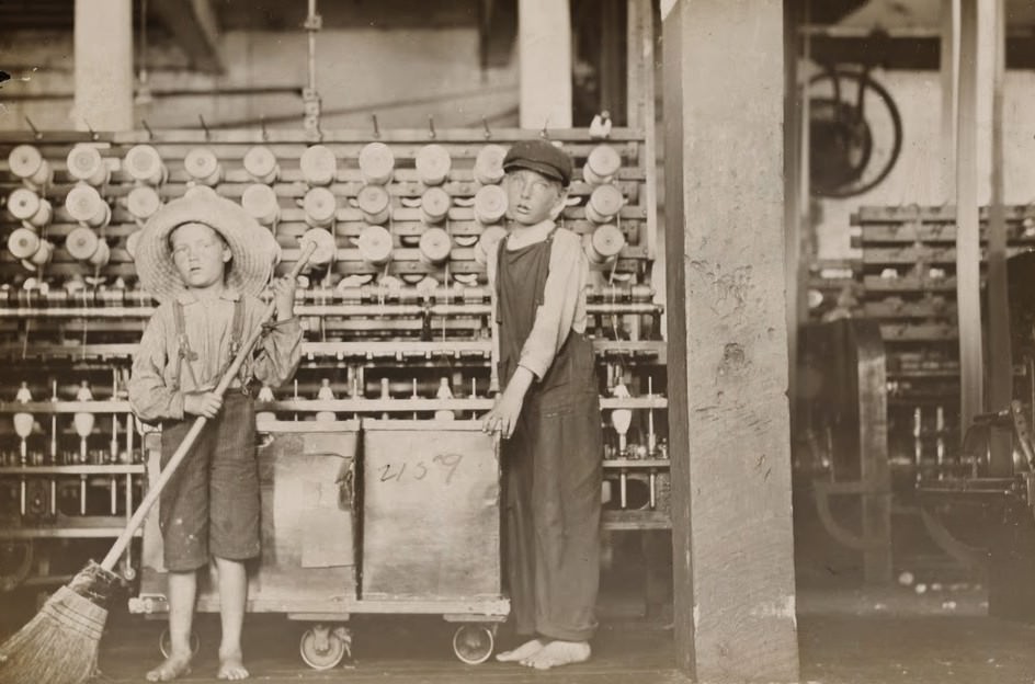 #8 Ronald Webb, twelve year old doffer boy and Frank Robinson, seven year old who helps sweep and doff. Father is cardroom boss, Roanoke (Va.) Cotton Mills. Roanoke, Virginia, USA, May 1911.