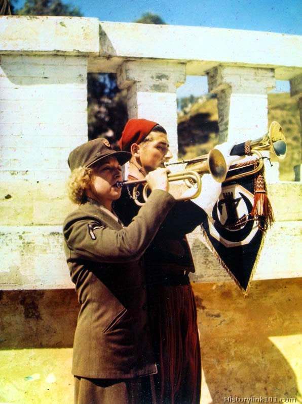 An American WAC and the bugler of the famous First Zouave Regiment of North Africa combine under Mediterranean skies to sound an Army call. At the left is a member of the historic first overseas company of the WAC which, in January 1944, will have completed a year of service in the North African Theater.
