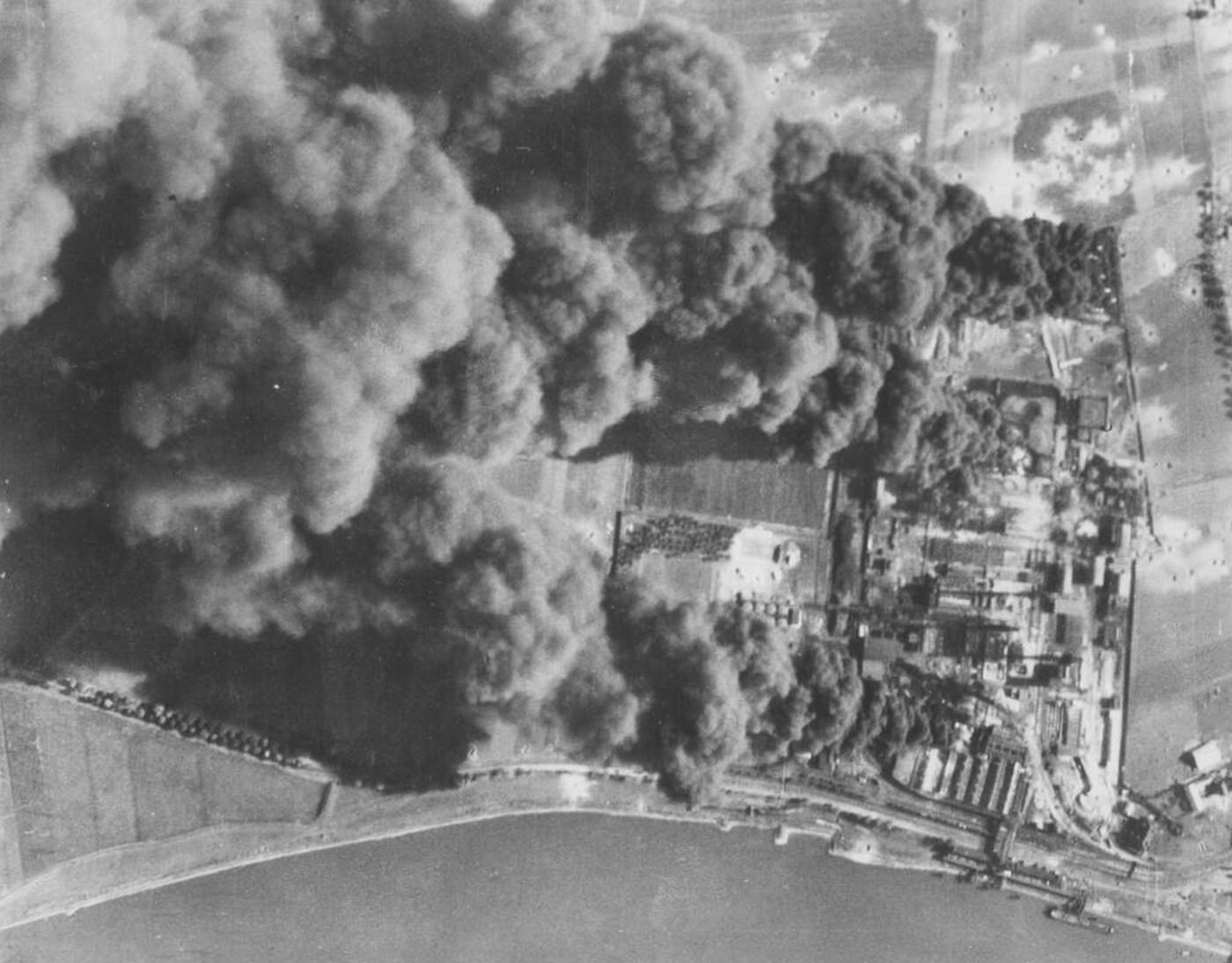 Flames burst through the black smoke from burning oil storage tanks and installations at the Nonheim oil refinery, 1945.