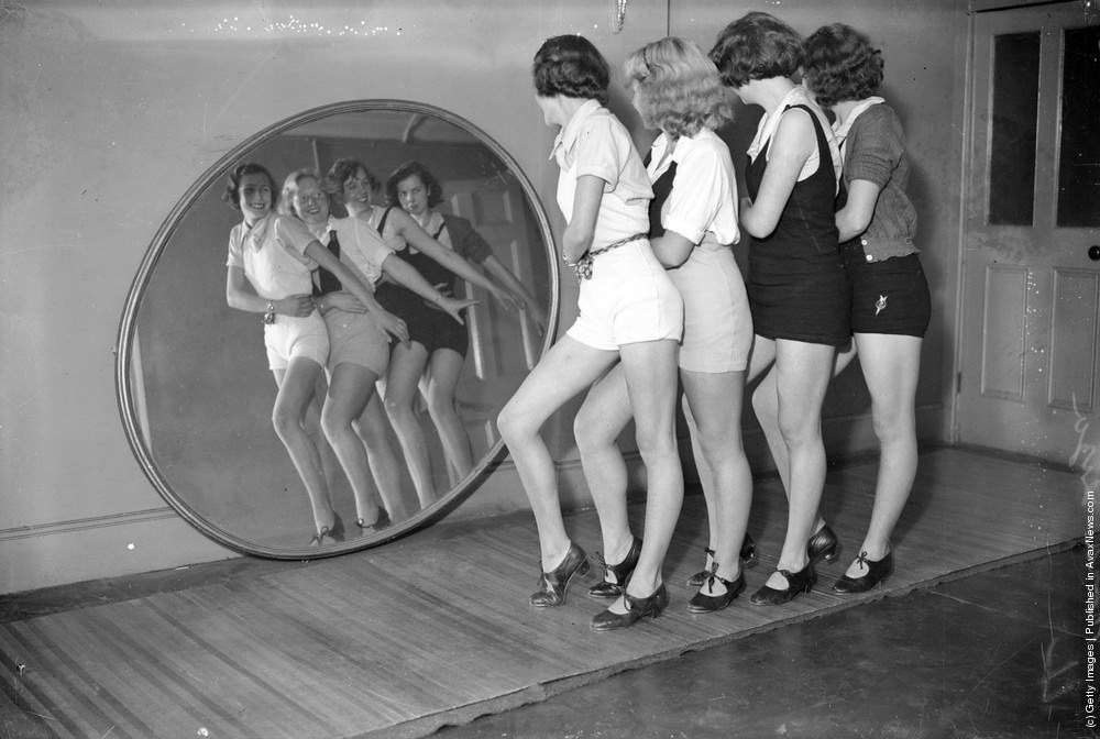 Students at a dance school dancing in front of a large, round mirror, 1935.