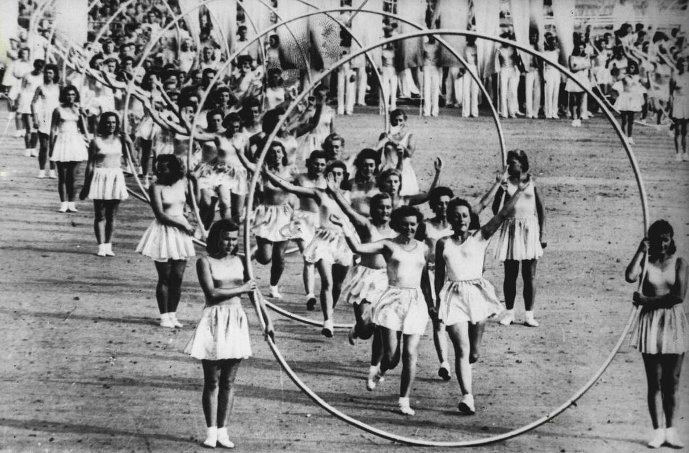 Girl gymnasts of the Trade Union Sport Societies tripping through hoops held by statuesque fellow-members as they take part in the All-Union Sport Parade at the Dynemo Stadium, Moscow, 1946.